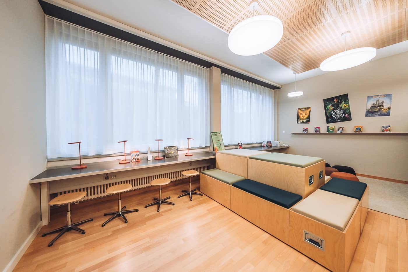 An einer Fensterfront in einem modernen Schulzimmer h&auml;ngen Tagesvorh&auml;nge und davor stehen Tischleuchten, damit man am breiten Fensterbrett arbeiten kann